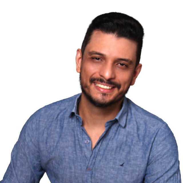 Foto de Heber Richard, um homem jovem, de pele branca, cabelos lisos e curtos e barba curta. Seus cabelos, barba e olhos são castanhos escuros. Ele usa uma camisa azul clara e sorri.